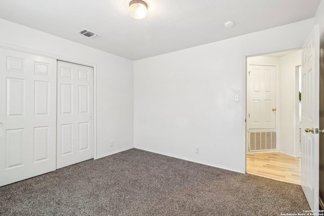 unfurnished bedroom featuring dark colored carpet, a closet, visible vents, and baseboards