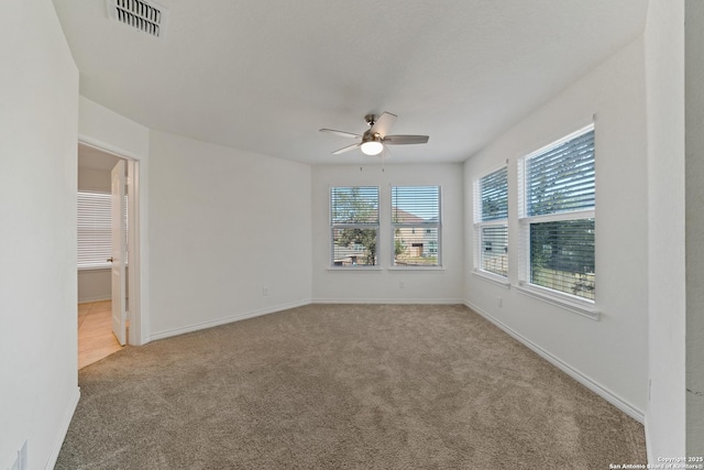 empty room featuring baseboards, a ceiling fan, visible vents, and light colored carpet