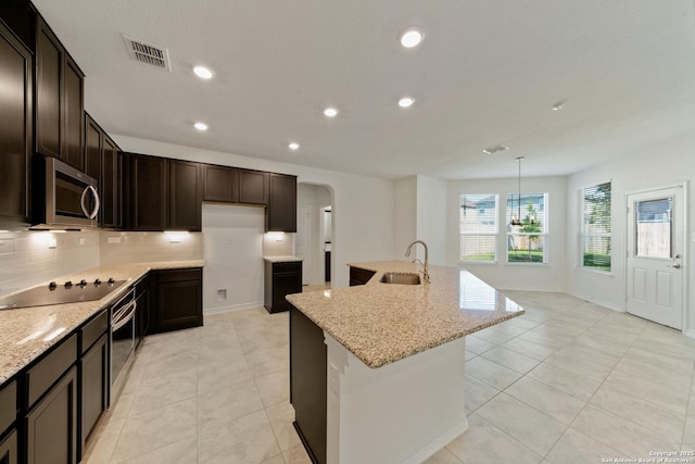 kitchen featuring arched walkways, light stone countertops, a kitchen island with sink, stainless steel appliances, and a sink