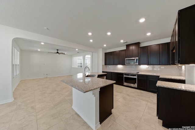 kitchen with backsplash, light stone countertops, a kitchen island with sink, stainless steel appliances, and a sink