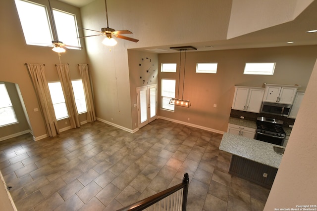 kitchen featuring stainless steel appliances, a high ceiling, white cabinetry, and baseboards