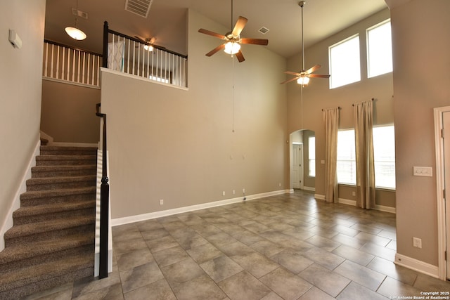 unfurnished living room featuring visible vents, arched walkways, ceiling fan, and stairway