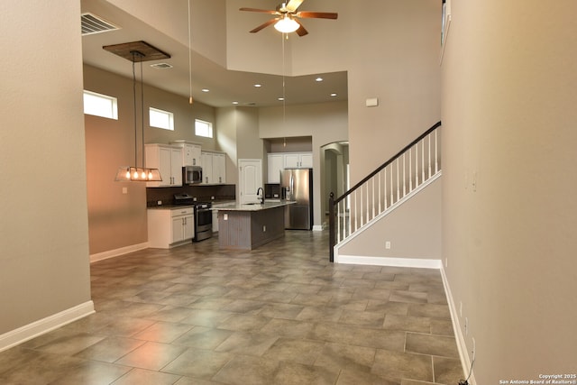 kitchen with decorative light fixtures, stainless steel appliances, visible vents, a kitchen island with sink, and white cabinetry