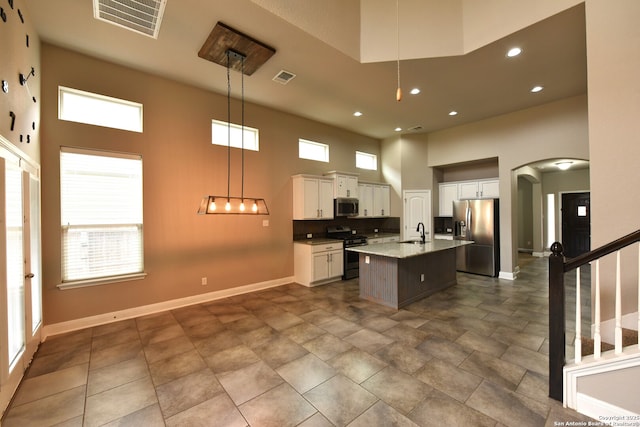 kitchen featuring pendant lighting, stainless steel appliances, a kitchen island with sink, a sink, and white cabinetry