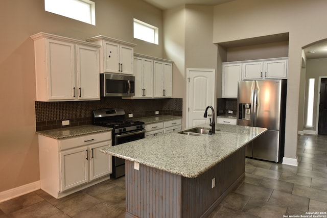 kitchen with light stone countertops, a center island with sink, appliances with stainless steel finishes, and a sink