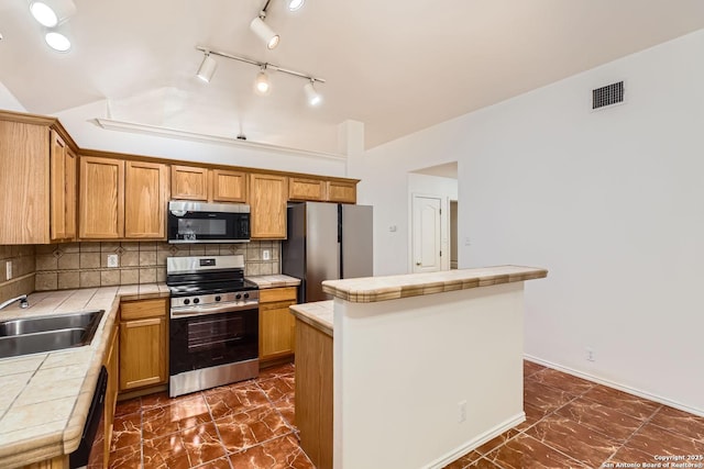 kitchen with a sink, a kitchen island, appliances with stainless steel finishes, and tile counters