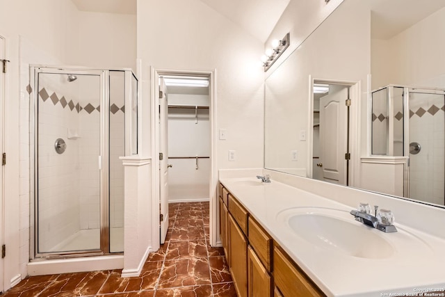 full bathroom featuring double vanity, a sink, a walk in closet, and a shower stall