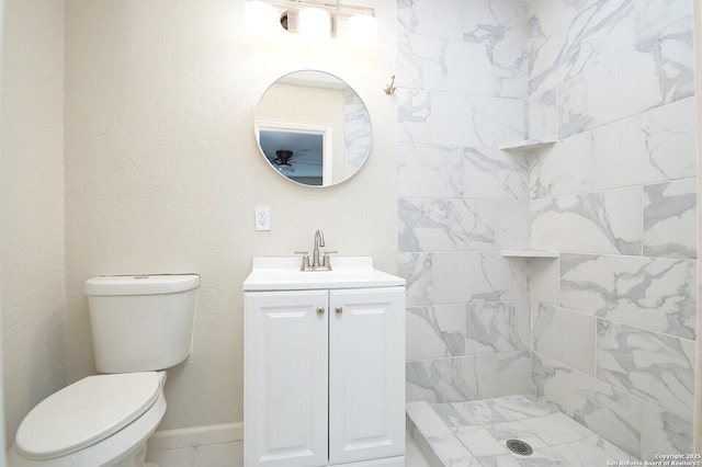 full bathroom featuring a tile shower, vanity, toilet, and baseboards