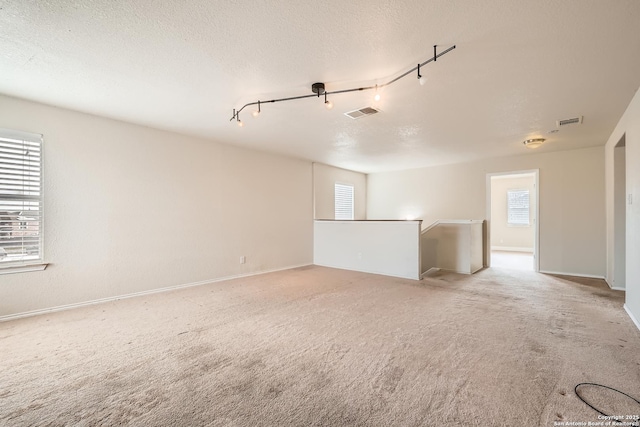 carpeted spare room featuring plenty of natural light, visible vents, and a textured ceiling