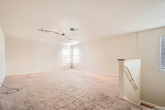 carpeted spare room featuring visible vents, a textured ceiling, and baseboards