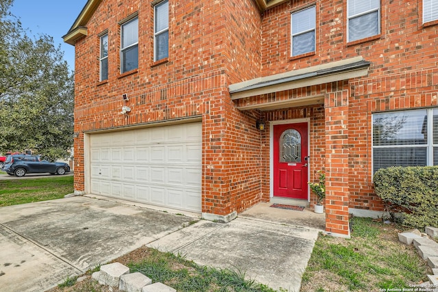 view of exterior entry with a garage, concrete driveway, and brick siding