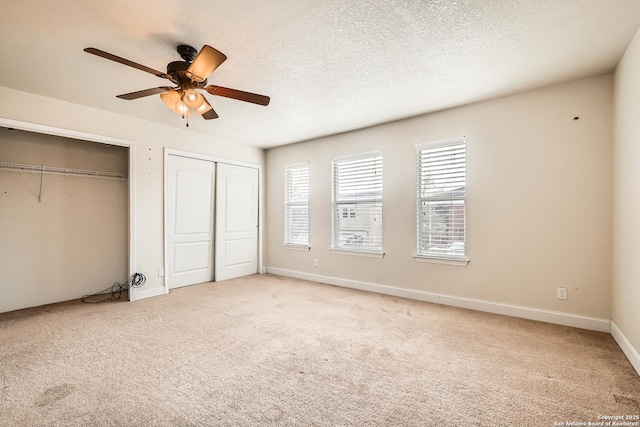 unfurnished bedroom with a textured ceiling, two closets, a ceiling fan, and light colored carpet