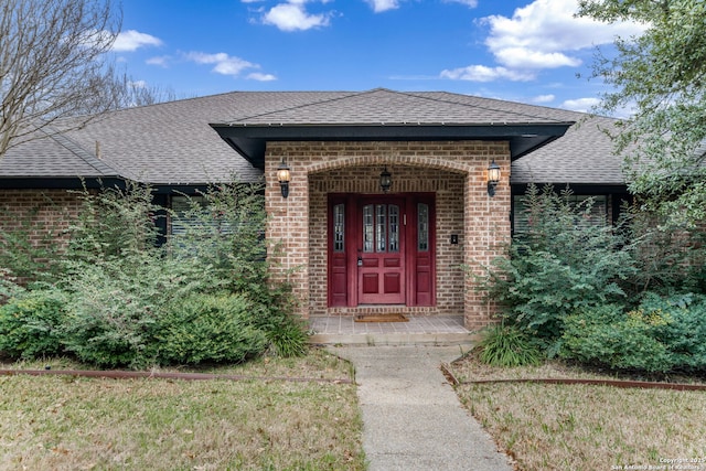 property entrance featuring a yard, roof with shingles, and brick siding