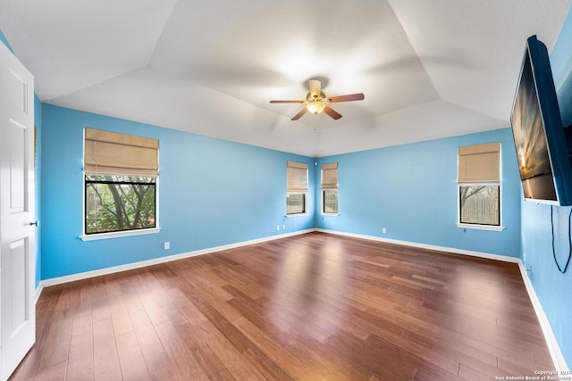 empty room with ceiling fan, lofted ceiling, wood finished floors, baseboards, and a tray ceiling