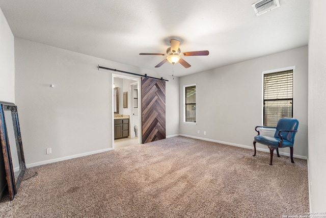 interior space featuring a barn door, visible vents, baseboards, ceiling fan, and carpet