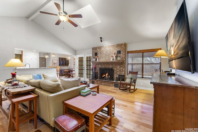 living room with ceiling fan, high vaulted ceiling, a fireplace, beam ceiling, and light wood finished floors