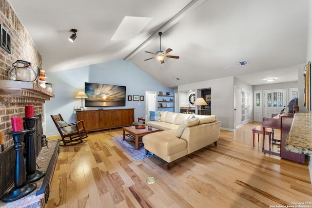 living area featuring vaulted ceiling with skylight, a fireplace, visible vents, a ceiling fan, and light wood-type flooring