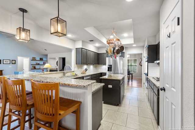 kitchen with stainless steel fridge, a peninsula, a tray ceiling, a kitchen bar, and a sink