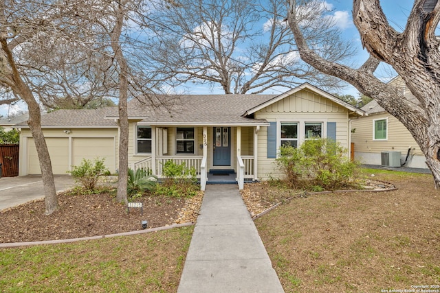 view of front facade featuring a shingled roof, covered porch, an attached garage, central AC unit, and a front yard