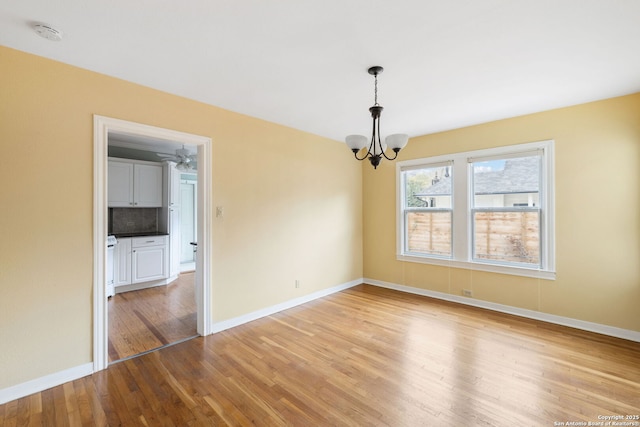 unfurnished dining area featuring light wood-type flooring, an inviting chandelier, and baseboards