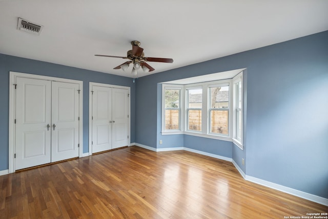 unfurnished bedroom featuring baseboards, visible vents, ceiling fan, wood finished floors, and multiple closets