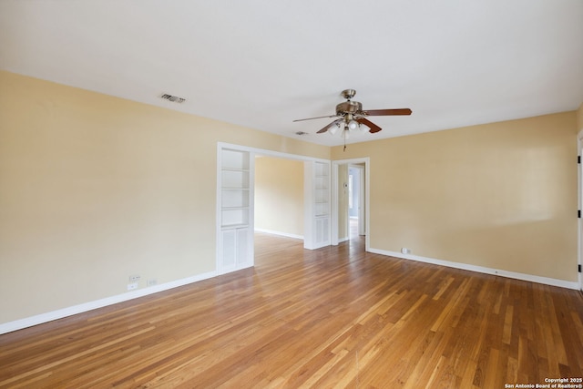 empty room featuring ceiling fan, wood finished floors, visible vents, and baseboards