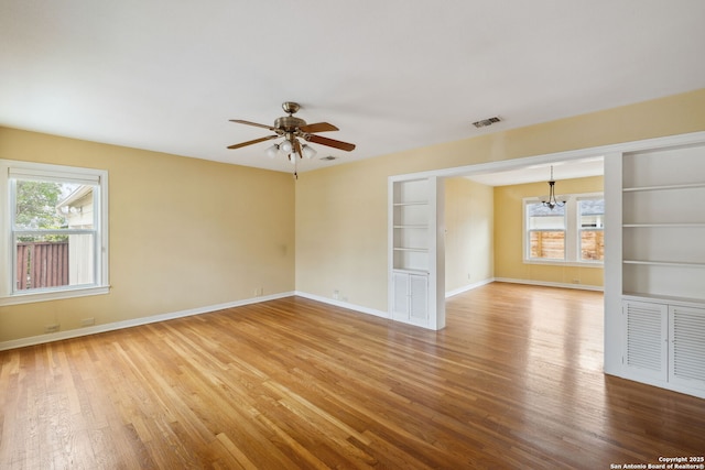 empty room with ceiling fan with notable chandelier, visible vents, baseboards, and wood finished floors