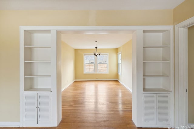 interior space featuring built in features, a chandelier, light wood-style floors, and baseboards