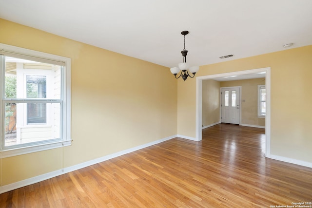 empty room featuring an inviting chandelier, baseboards, visible vents, and wood finished floors