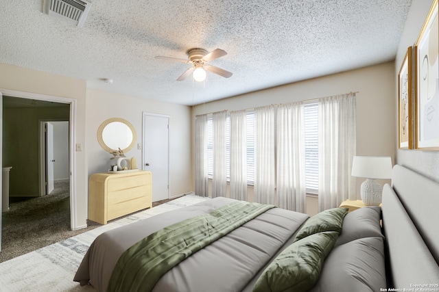 bedroom featuring a textured ceiling, carpet floors, visible vents, and a ceiling fan