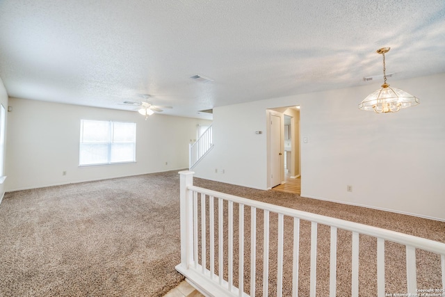 unfurnished room featuring light carpet, visible vents, a ceiling fan, stairs, and a textured ceiling