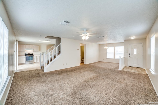 unfurnished living room with light carpet, visible vents, a ceiling fan, stairs, and a textured ceiling