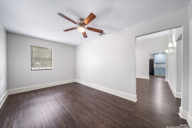 spare room featuring dark wood-style floors, ceiling fan, visible vents, and baseboards