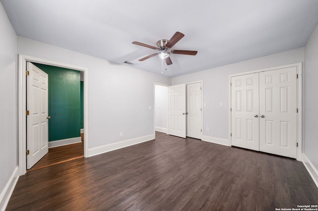 unfurnished bedroom featuring dark wood-style floors, baseboards, visible vents, and multiple closets