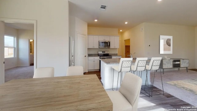 kitchen featuring a center island with sink, appliances with stainless steel finishes, light stone countertops, a kitchen bar, and white cabinetry