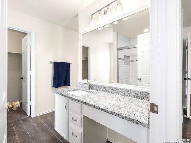 bathroom with a spacious closet, wood finish floors, vanity, and a stall shower