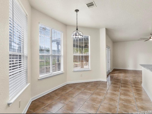 unfurnished dining area featuring baseboards, visible vents, tile patterned floors, a textured ceiling, and ceiling fan with notable chandelier