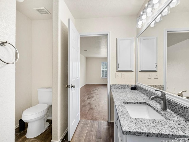 bathroom with a textured ceiling, toilet, visible vents, vanity, and wood tiled floor