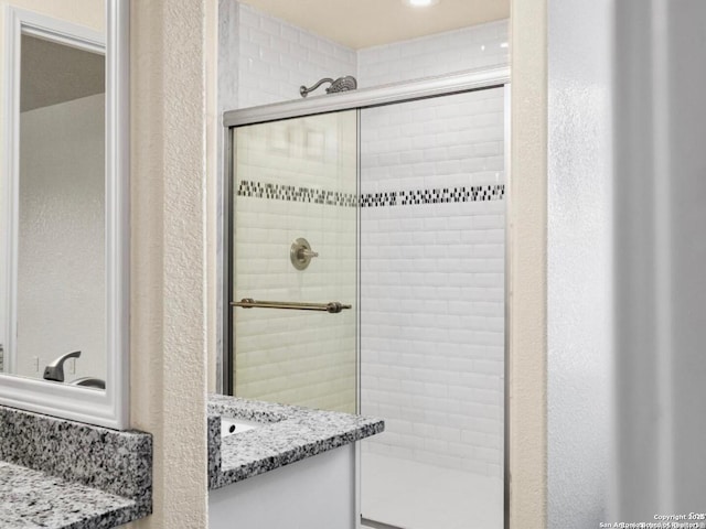 bathroom with a textured wall, a shower stall, and vanity