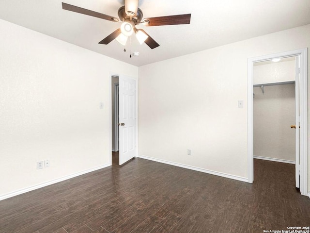 unfurnished bedroom featuring dark wood-type flooring, a closet, a spacious closet, and baseboards