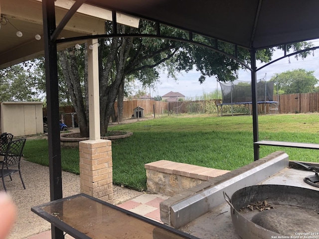 view of yard with a fenced backyard, a fire pit, an outdoor structure, a storage unit, and a trampoline