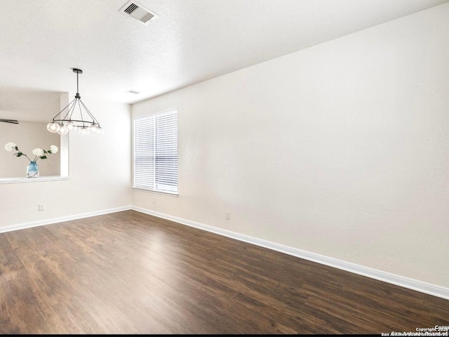 unfurnished room with dark wood-style flooring, visible vents, a notable chandelier, and baseboards