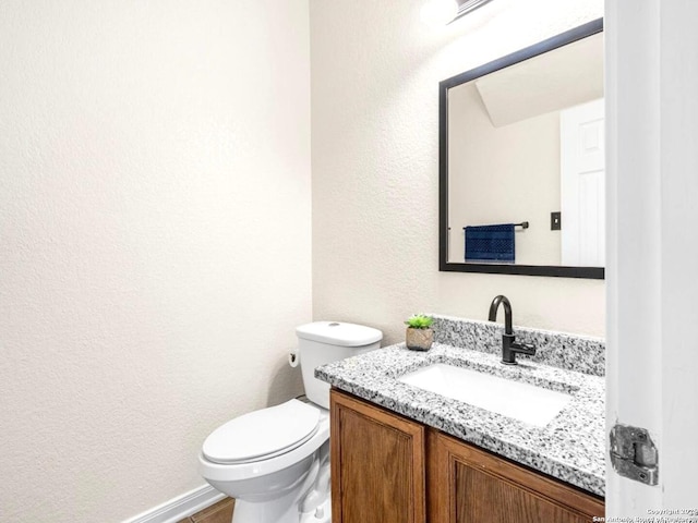 half bathroom featuring toilet, a textured wall, and vanity