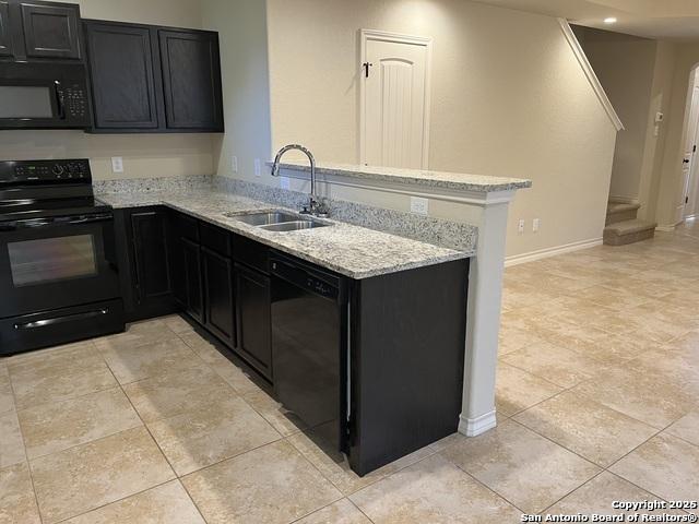 kitchen featuring a peninsula, light stone countertops, dark cabinetry, black appliances, and a sink