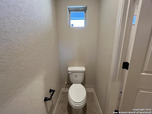 bathroom with baseboards, a textured wall, and toilet