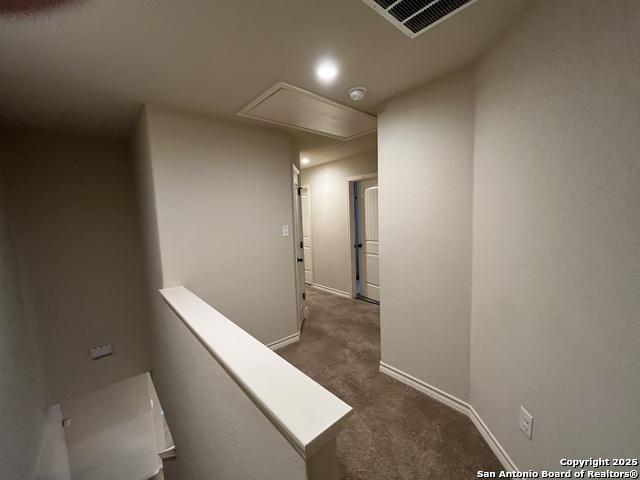 corridor with attic access, visible vents, baseboards, an upstairs landing, and dark carpet