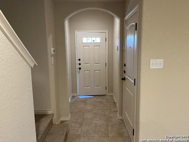 doorway with arched walkways, light tile patterned floors, and baseboards