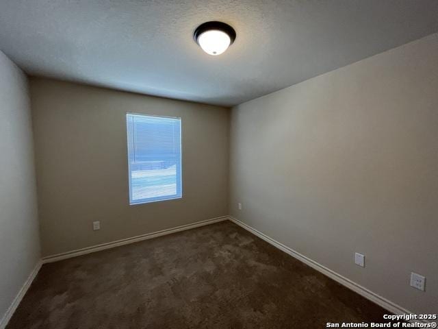 spare room featuring baseboards, dark colored carpet, and a textured ceiling