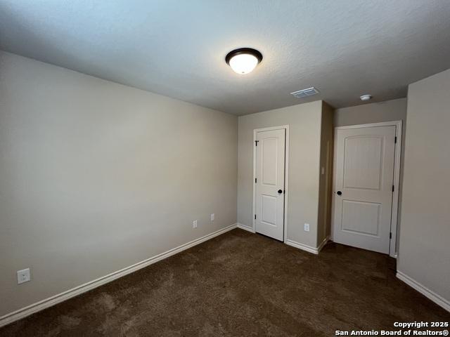 unfurnished bedroom with dark colored carpet, visible vents, and baseboards