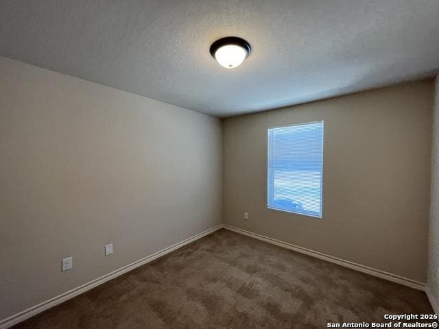 spare room with dark carpet, a textured ceiling, and baseboards